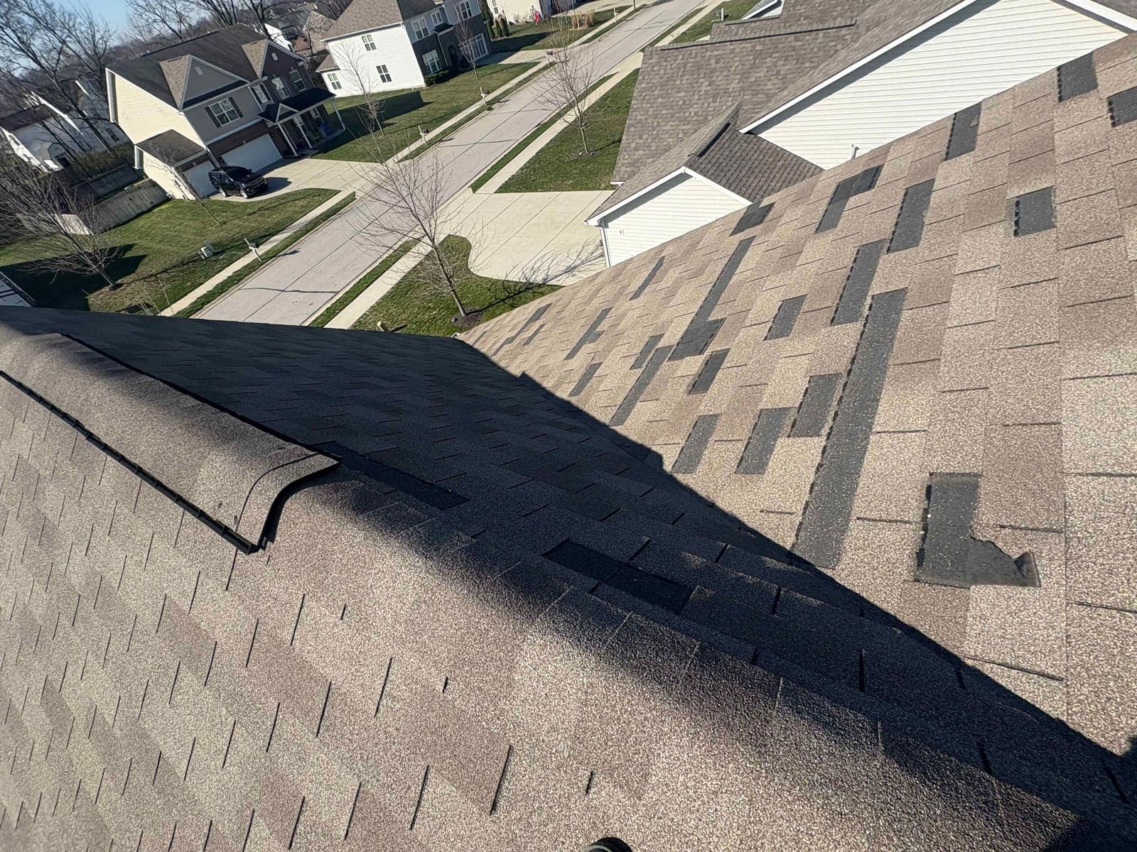 Roof slope with multiple shingle tabs torn off by wind, exposing dark underlayment