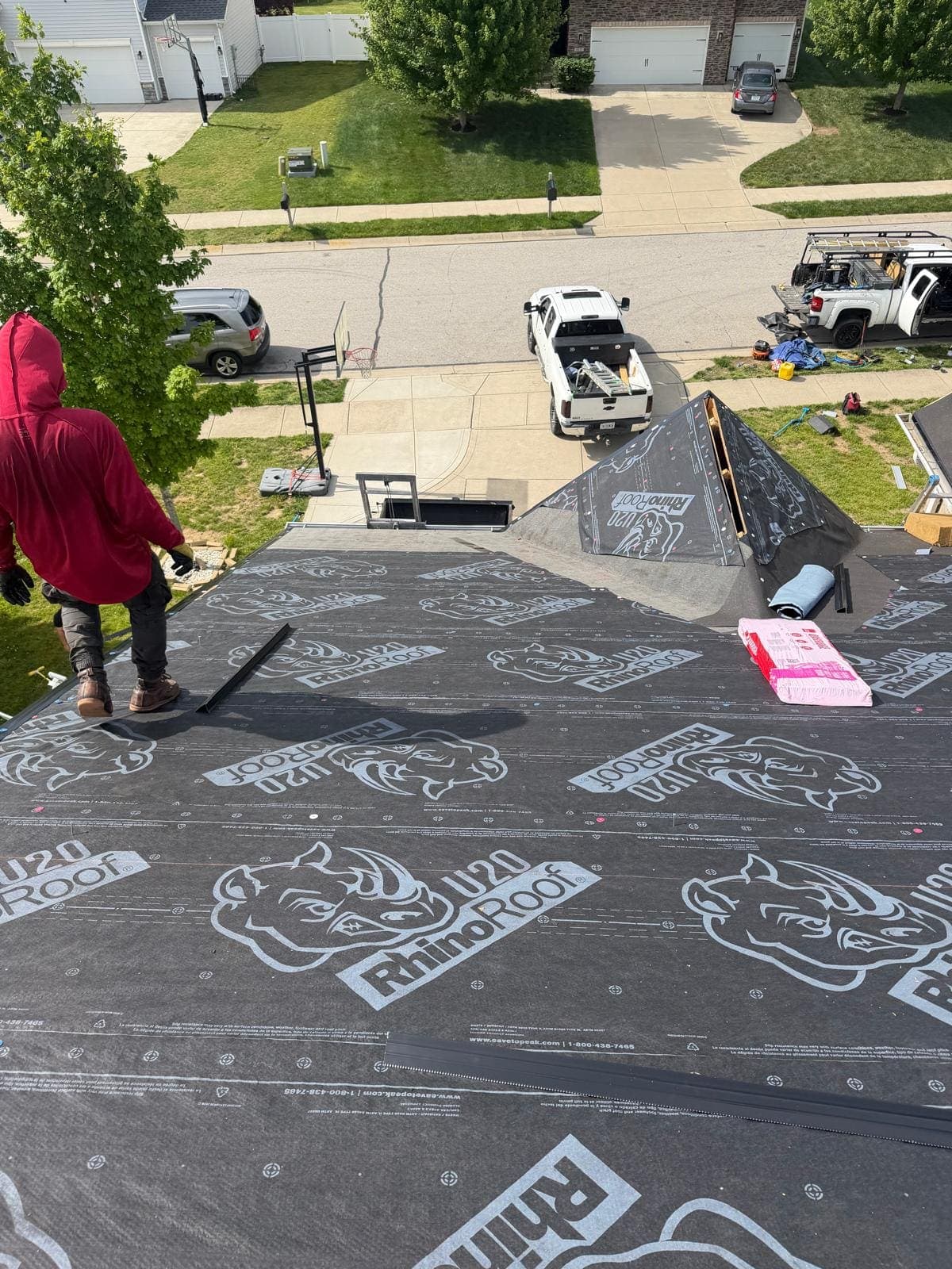 Checkered Flag Roofing crew member on a dried-in roof with the company trucks parked on the street below in Avon, Indiana