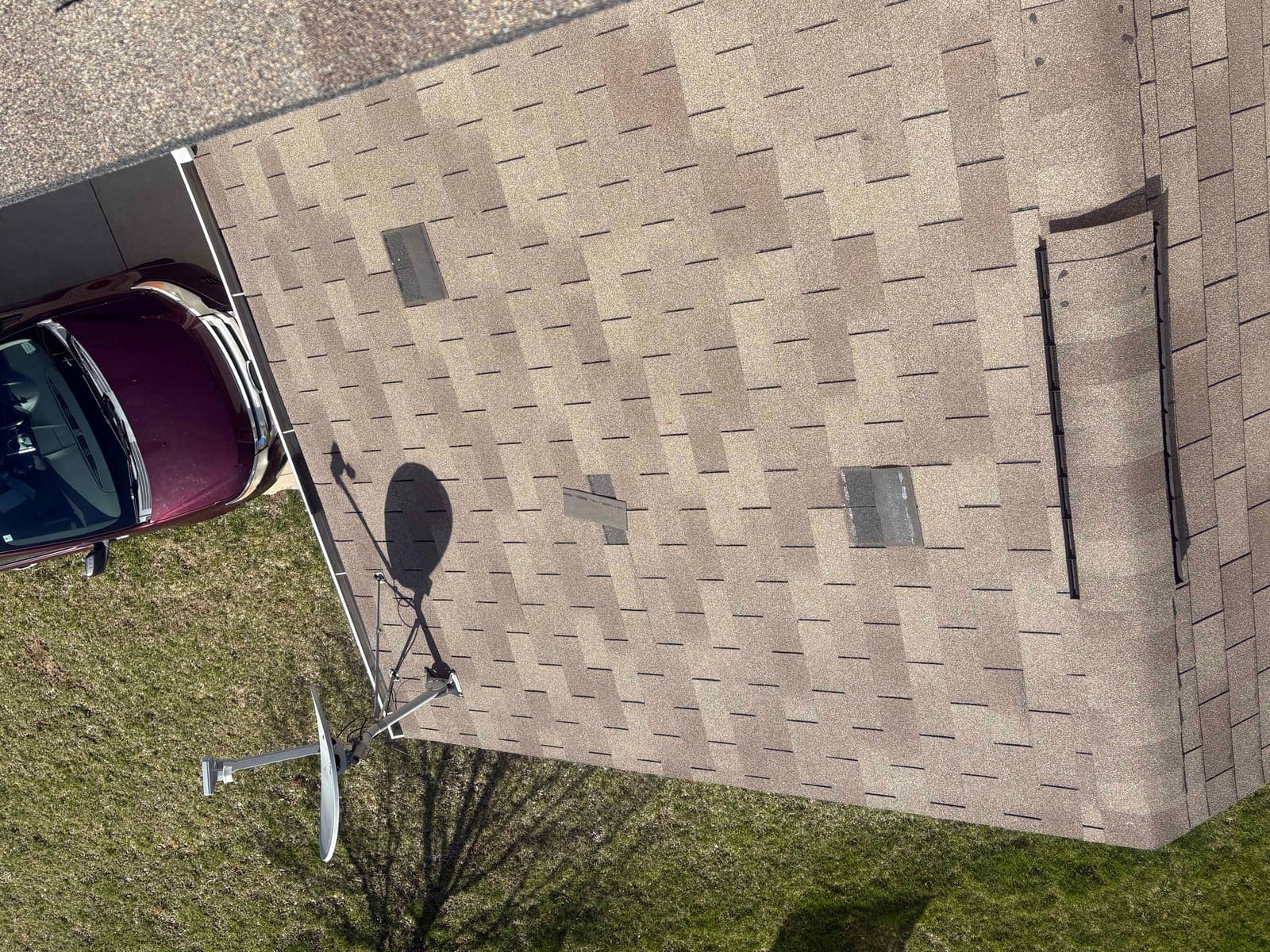 Roof slope beside a satellite dish with several shingle tabs missing and underlayment exposed, storm damage documentation in the Carmel area