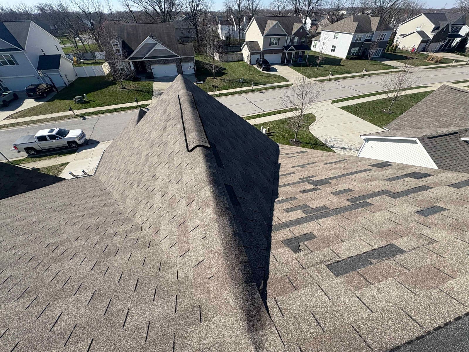 View along a roof ridge showing scattered missing shingles on the slope below, houses and street in the background, in the Lebanon area of Boone County