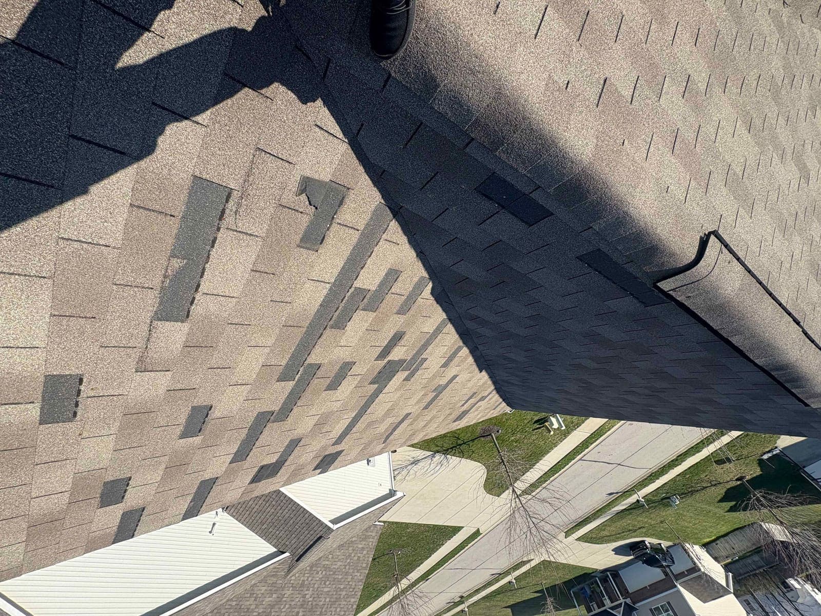 Steep roof slope photographed from above showing widespread missing shingle tabs, near Sheridan in the warned area